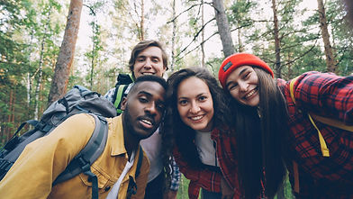 A biracial group of men and women in the woods, wearing hiking hear and smiling at a camera.
