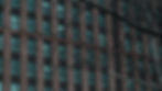 Brick building with teal windows, bare tree branches in foreground. Overcast mood, no visible text or people. Urban setting.