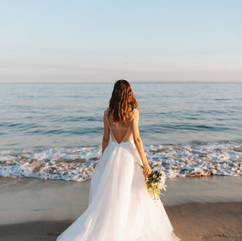 Bride in white gown facing the ocean with a bouquet