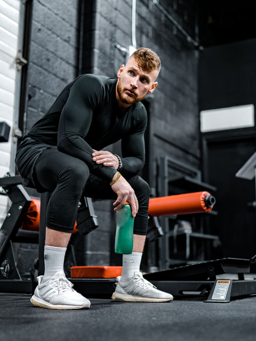 Man in gym clothes resting on a machine with a water bottle