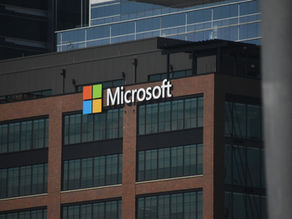 Microsoft logo on a brick building with large windows. The colorful logo stands out against the corporate, modern facade.