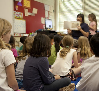 Kinder sitzen in der Schule. Lehrerin liest vor.