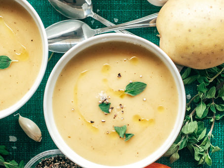 Bowls of creamy loaded potato soup garnished with fresh herbs and cracked pepper, set alongside fresh ingredients and utensils on a green background.