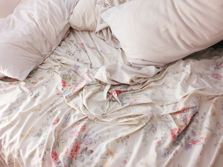 A softly lit messy bed with tangled sheets and pillows, symbolizing intimacy, connection, passion, and the emotional aftermath of partnered sex.