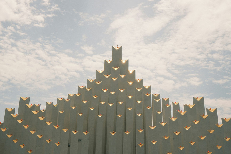 Geometric structure with symmetrical peaks under a cloudy sky. Sunlight reflects off edges, creating a serene and grand visual effect.