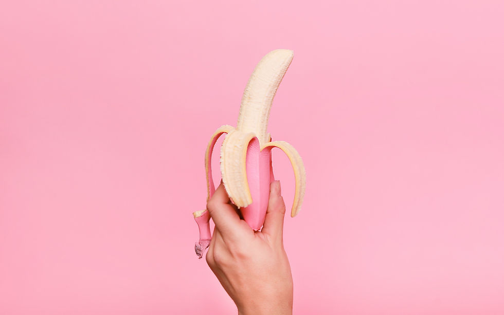 A hand holding a pink skinned banana on a pink background