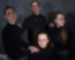Family, codependency,four people in black turtlenecks and glasses pose against a dark gray background, hands resting on each other's shoulders, creating a formal mood.
