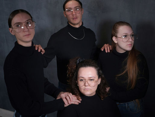 family, codependency, four people in black turtlenecks and glasses pose against a dark gray background, hands resting on each other's shoulders, creating a formal mood.