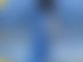 Gen z female with long, wavy dark brown hair is posing stylishly in front of a wall painted with blue and yellow graffiti. She is wearing a black and white crochet top with long blue jeans.