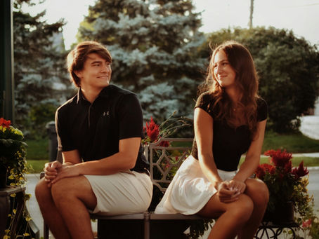a man and woman chatting seaside while sitting on a short log fence