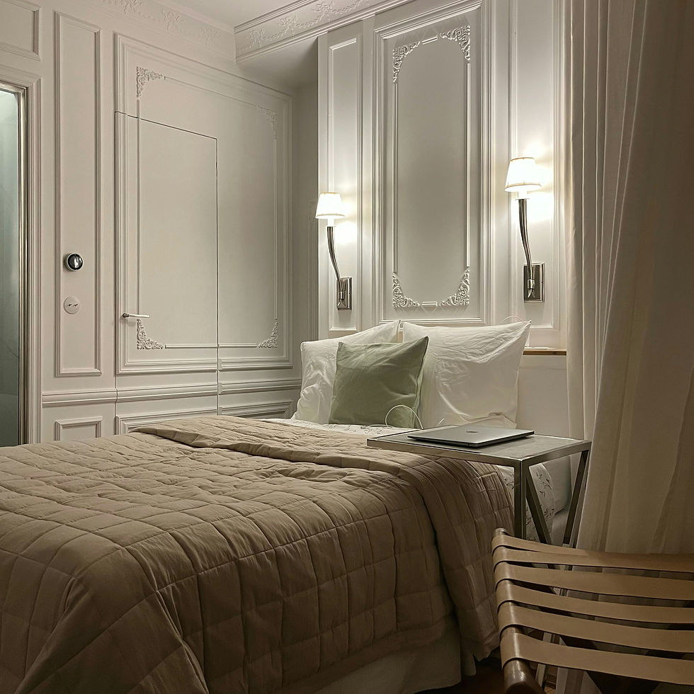 Elegant bedroom with beige quilt, white pillows, and a sage cushion. Two wall lamps illuminate the ornate paneling. Calm and inviting mood.