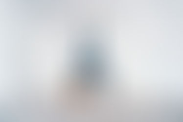 Yogini in blauem Outfit übt das ganze Rad mit gestreckten Bein nach oben. Sie befindet sich zwischen weissen Arkaden