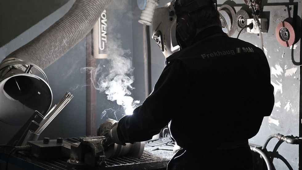 Worker welding metal in an industrial shop, sparks and smoke rising.