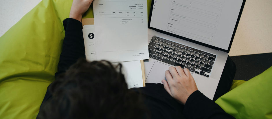 Looking down on a person using a laptop and looking at invoice paperwork
