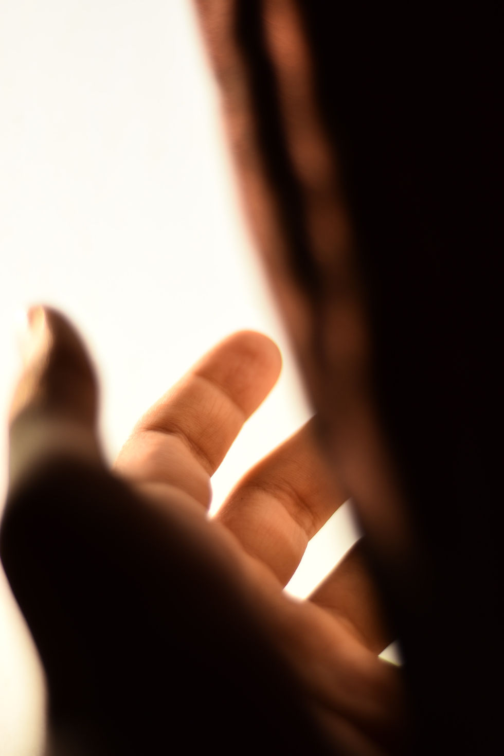 Close-up of a hand with fingers reaching towards a softly lit background. The image is warm-toned, creating an introspective mood.
