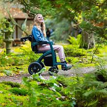 young person using a power wheelchair through a park setting
