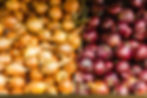 Boxes of yellow and red onions are displayed side by side. The onions are unpeeled, with vibrant colors contrasting each other.
