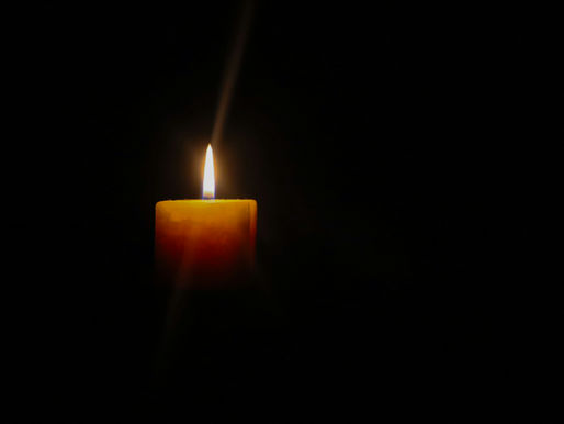 Lit candle glowing in the dark with a soft, warm flame against a black background, creating a calm and serene atmosphere.