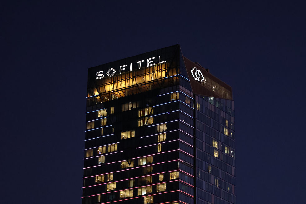 Nachtansicht eines modernen Hochhauses mit leuchtendem SOFITEL-Schriftzug und pink-blauen Lichtstreifen am Glasbau.