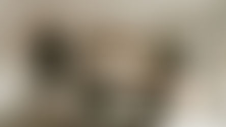 Minimalist kitchen with wooden cabinets, gray table, and chairs. Open book, plant, candle, and stainless steel fridge in bright, airy room.