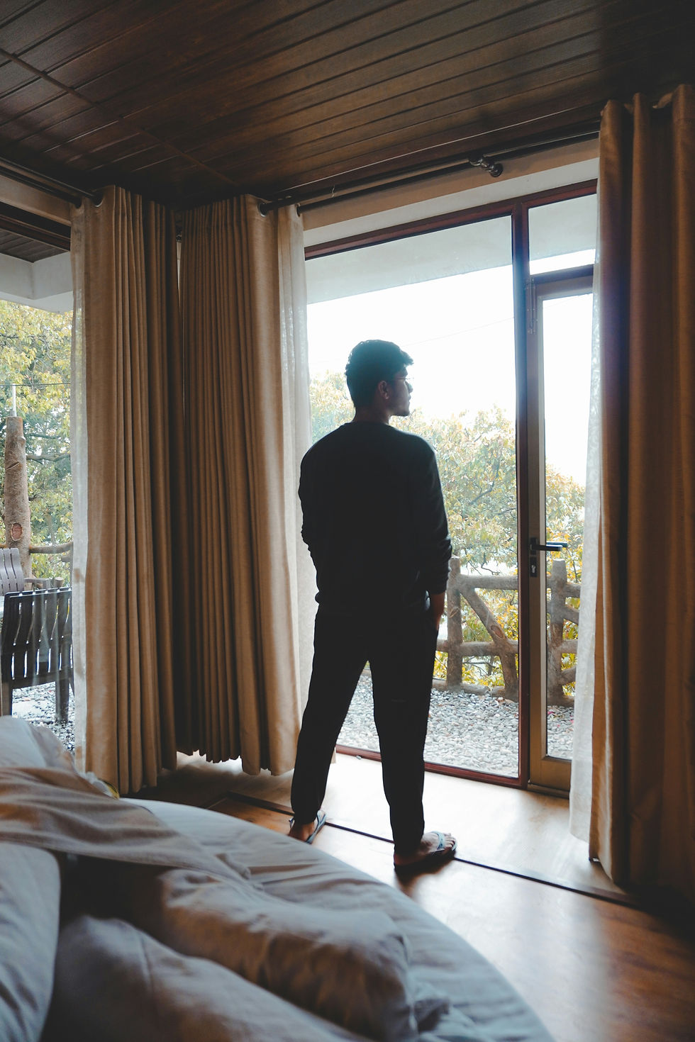 Man standing looking out of a big window. Looking at him from the back, his knees are locked backwards.