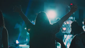 Silhouette of a person raising arms at a concert. Blue lights illuminate the crowd, creating an energetic and uplifting atmosphere.