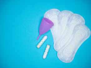 3 period pads, 2 tampons and a moon cup against a blue background