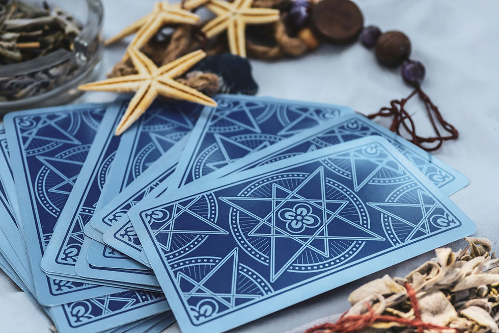 Blue patterned cards fanned on a white surface, surrounded by starfish, shells, and beads, suggesting a calm seaside tarot setup
