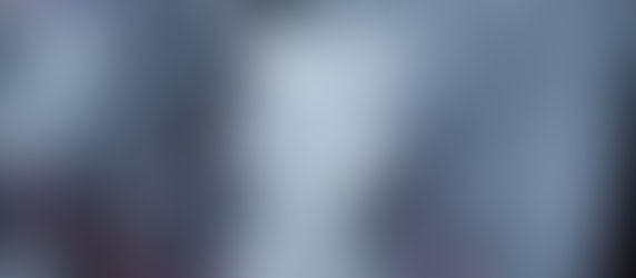 A vibrant Hindu deity statue adorned with intricate silver designs stands amidst smoke. The colorful headpiece and piercing gaze create a dramatic aura.