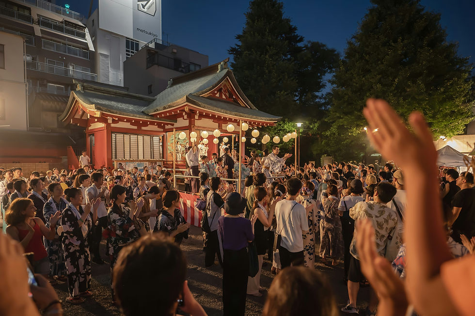 Crowd gathers at a lively evening festival near a lit pavilion adorned with paper lanterns. People in traditional attire clap joyfully.
