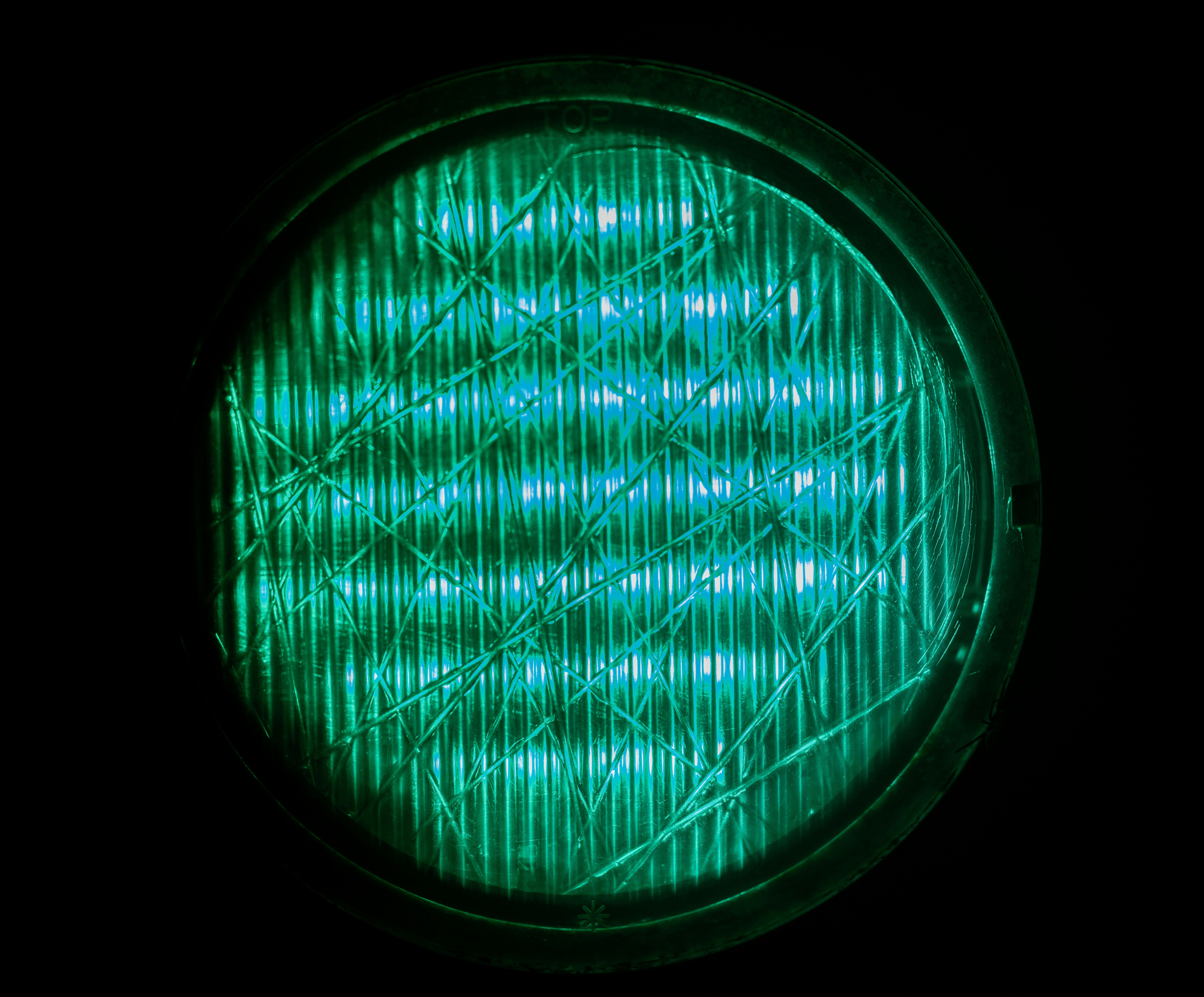 Glowing green-blue circular light lens on black background, with faint OP text and geometric grid texture.