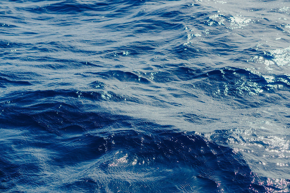 Waves ripple across a deep blue ocean under sunlight, creating shimmering reflections and a tranquil, serene atmosphere.