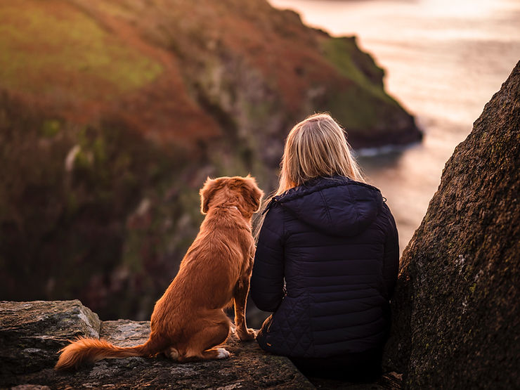 Woman sits with a happy Gdog on a cliff. She actively works with her dogs meridian clock to keep him healthy.