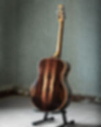 Rosewood guitar on a stand in a vintage room with worn walls and floor. Warm wood tones contrast with the muted background, creating a rustic vibe.