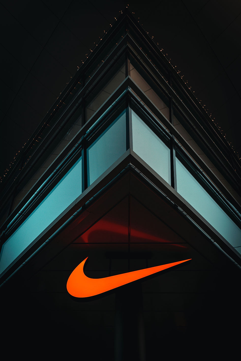 Building corner with blue-tinted glass, black sky, and orange illuminated swoosh logo near the bottom. Calm and modern atmosphere.