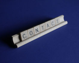 Wooden letter tiles spelling CONTACT on a blue background, arranged on a small white holder.