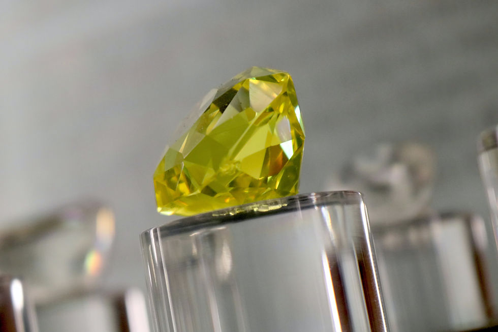 A yellow gemstone with facets rests on a clear stand, set against a blurred gray background. The scene is serene and elegant.