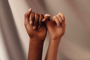 Two hands with different skin tones link pinkies in a gesture of connection. Soft, neutral background; conveys unity and friendship.