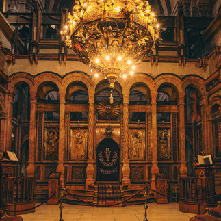 Interior view of a Greek Orthodox church in Jerusalem. A wide photo capturing the rich gold and dark wood ornate iconostasis (altar screen) and a large central chandelier, showcasing traditional religious art.
