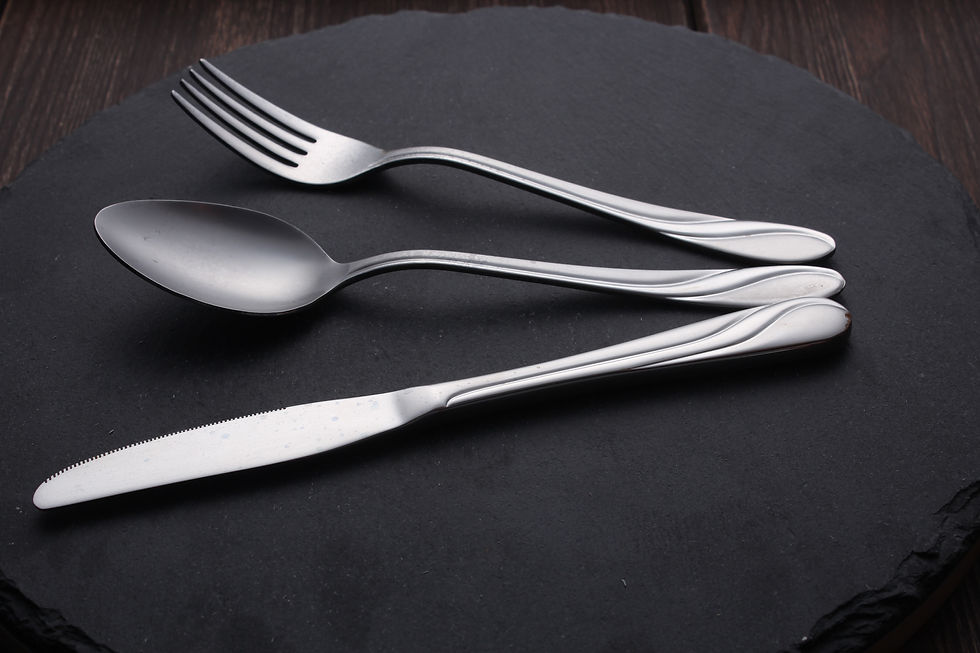 Silver fork, spoon, and knife on a dark slate surface. Wooden background adds a rustic touch. Simple, elegant design.
