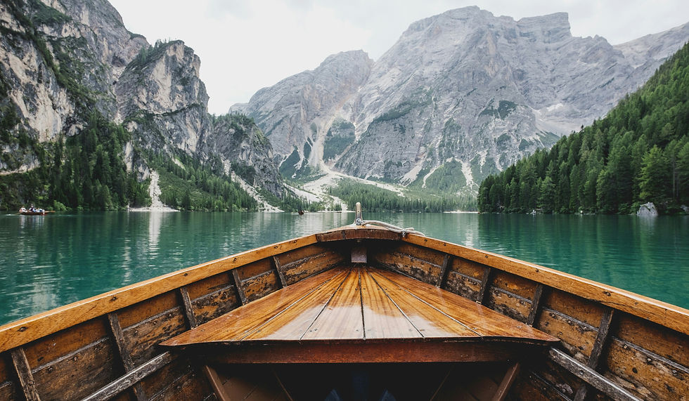 A serene view of a lake from a wooden boat, surrounded by lush greenery and a clear blue sky.