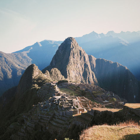 Machu Picchu at sunrise, with ancient stone structures and terraces in the foreground. Huayna Picchu mountain rises in the background.