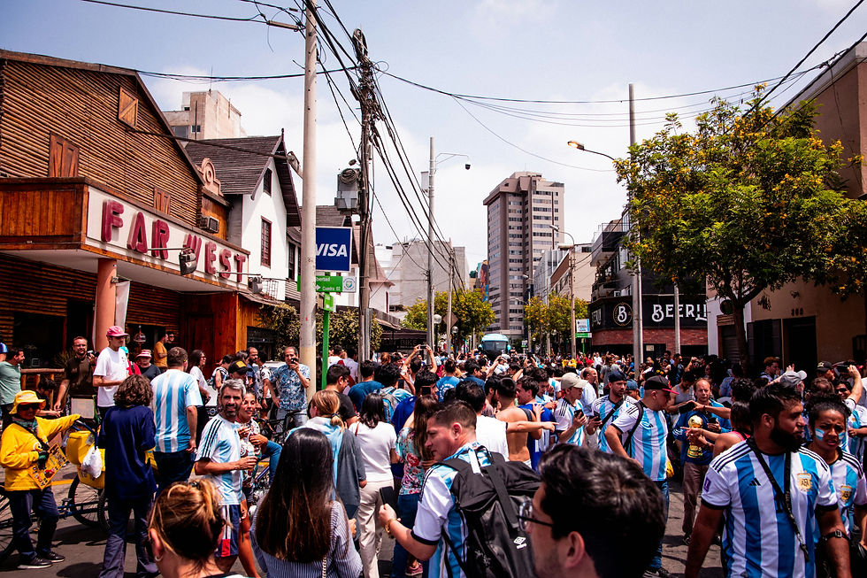 Multitud de personas con camisetas del equipo de Argentina celebrando en una calle urbana, junto a edificios y árboles. Ambiente festivo.