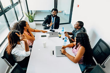 A picture of a group of people sat around a large table in a bright boardroom with large windows
