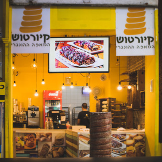 The bright yellow storefront of a traditional Hungarian Kurtosh bakery in Tel Aviv, specializing in chimney cakes.
