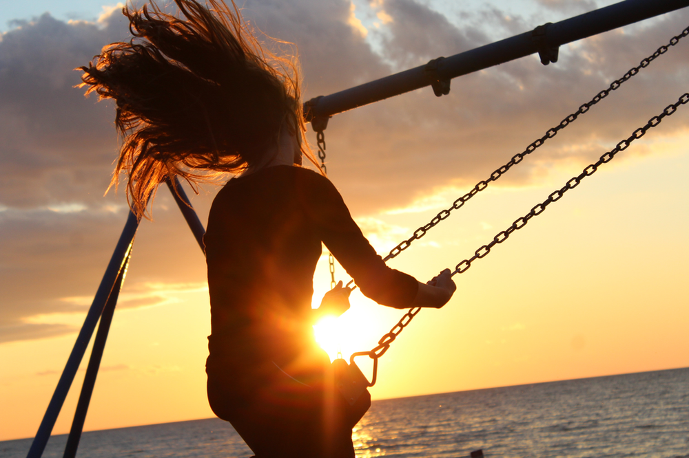 Silhouette of girl on swing-set near beach at sunset