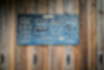 Blue board displaying various rope knots with labels, mounted on a wooden wall. Knots form intricate patterns against natural wood tones.