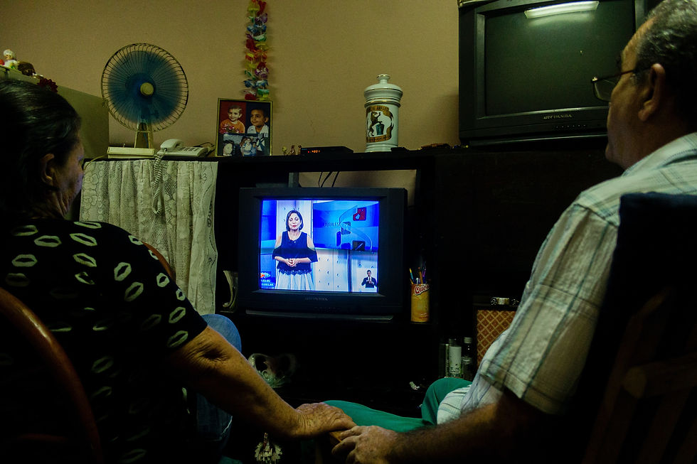 Photo of a couple watching TV in their home while holding hands.