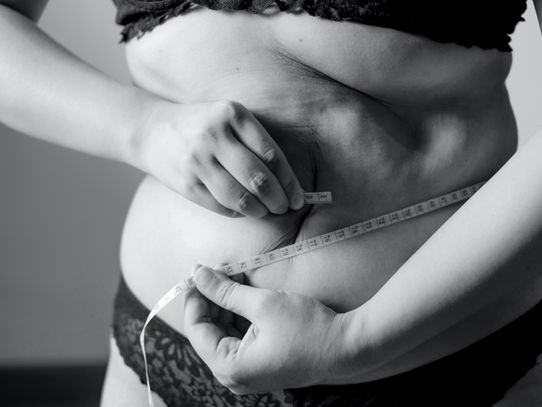 Woman standing on a scale at home, checking her weight as part of a healthy, sustainable weight-loss journey focused on hormones and metabolism.