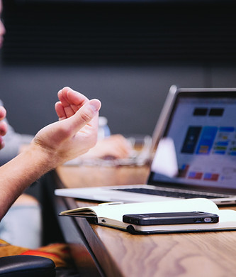 Man gesturing during meeting with laptop, notebook, and phone on the table.